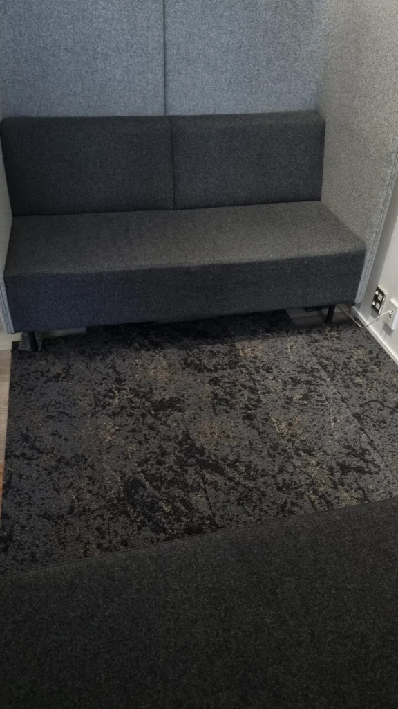 Dark patterned carpet tile flooring beside a grey bench seat